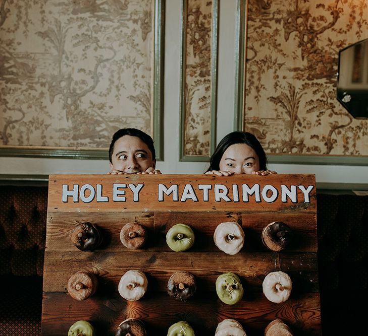 Bride and groom peeping over their DIY doughnut wall