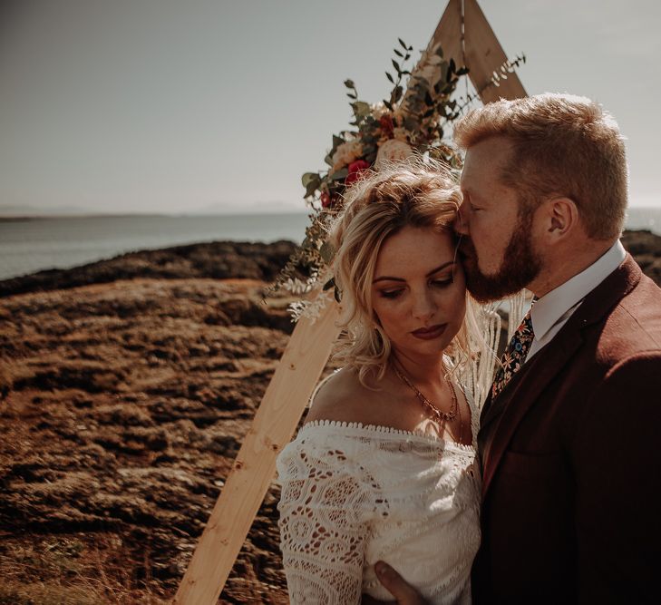 Bride and groom pose in front of wooden beams with floral decals of roses and assorted pink and green foliage 