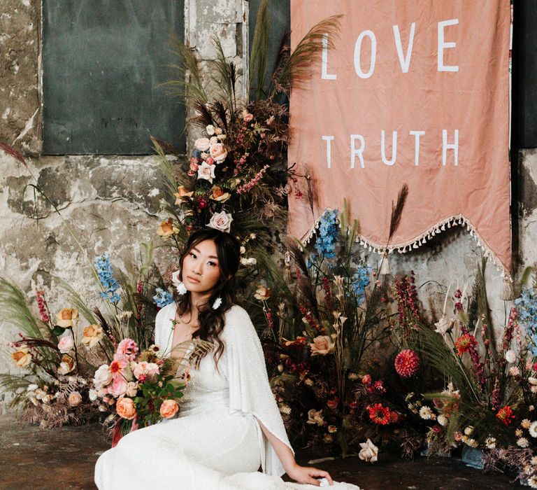 Bride in white sparkly wedding dress sitting at the altar surrounded by colourful flowers 