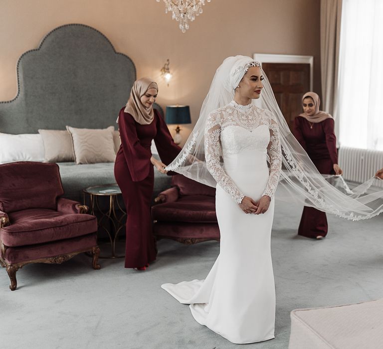 Bridesmaids in maroon dresses fanning out the brides veil