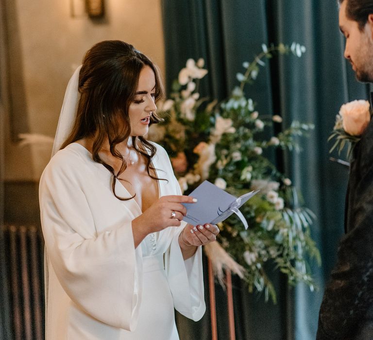 Bride holding order of service with silk wedding gown, white painted nails and diamond wedding ring