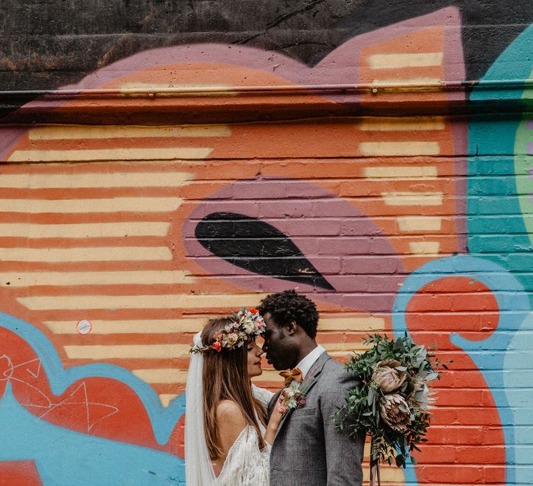 Bride and groom stand close in front of graffiti wall