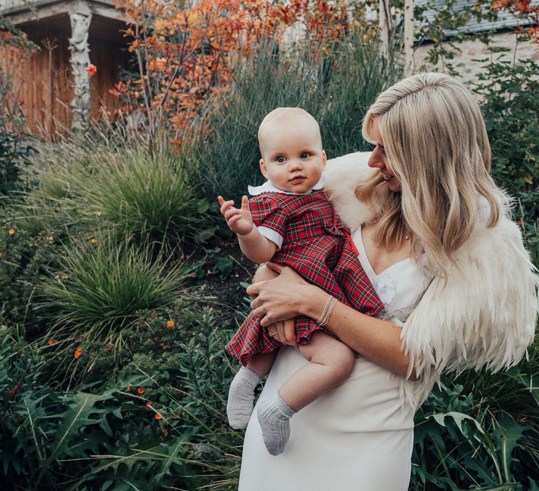 Bride holds baby wearing Tartan dress on wedding day 