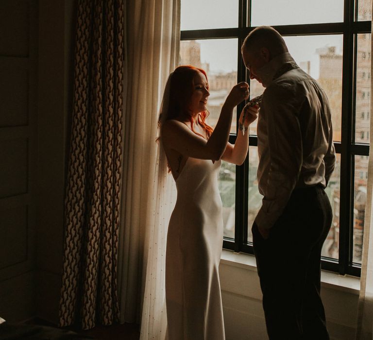 Bride tying husbands tie wearing a silk wedding dress 