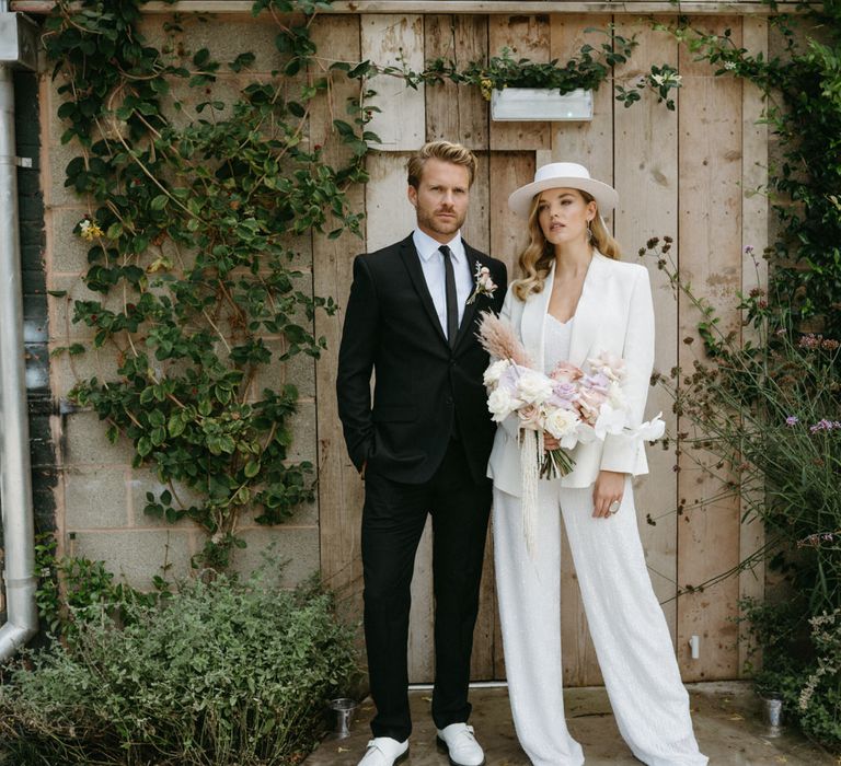 bride in a wedding jumpsuit and bridal hat holding a pastel tropical bouquet 