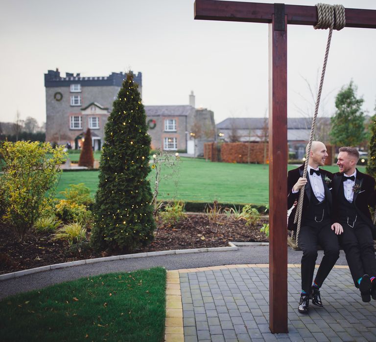 Two grooms in tuxedos sitting on a swing at Darver Castle Estate 