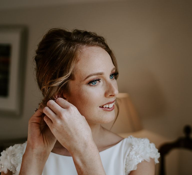 Red headed bride putting on her earrings on the wedding morning 