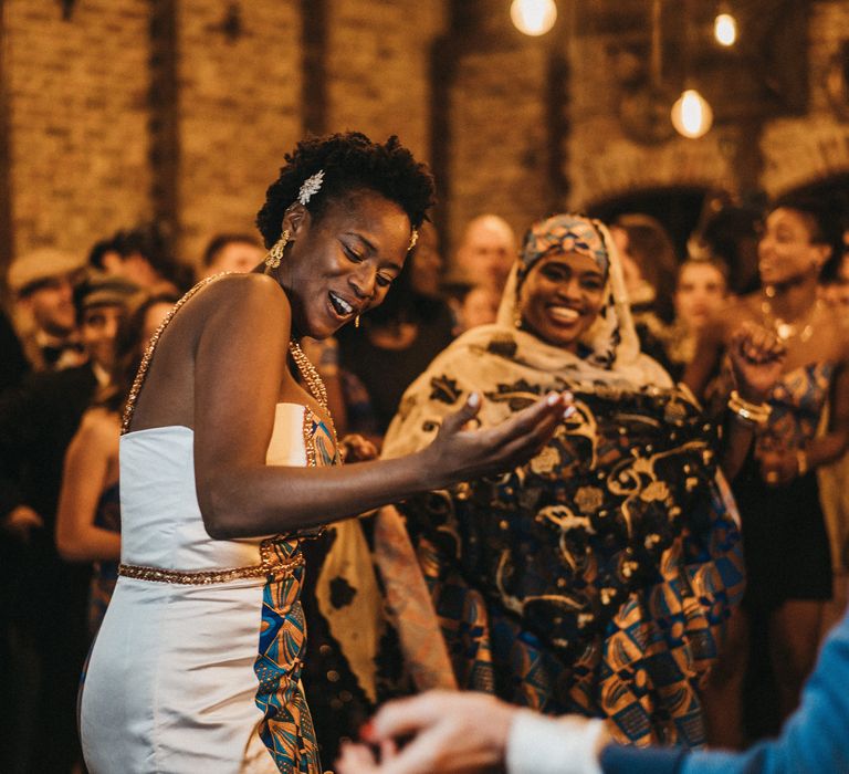 West African bride with short hair dancing in traditional outfits with blue tribal print and one shoulder detail