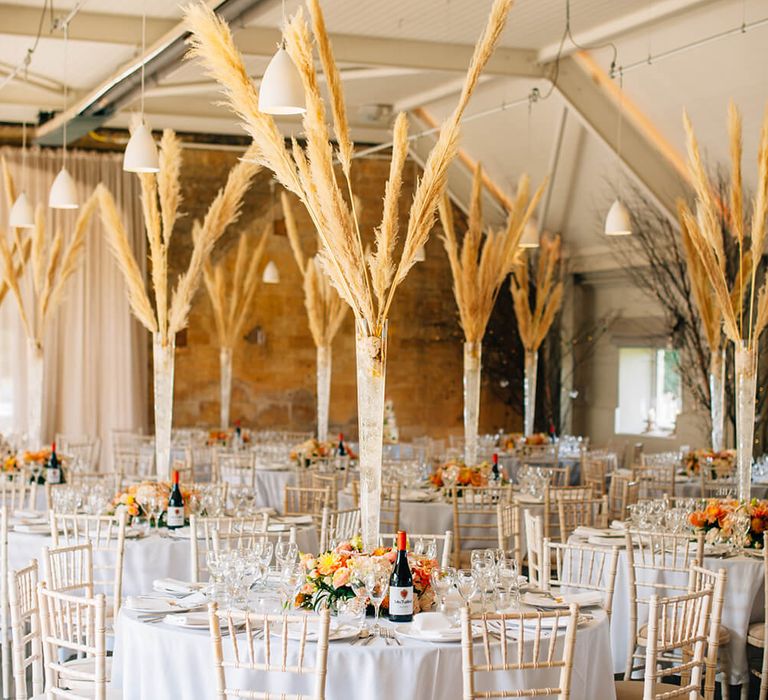 Peach citrus wedding centerpiece with pampas grass. White wedding chairs and table for barn wedding