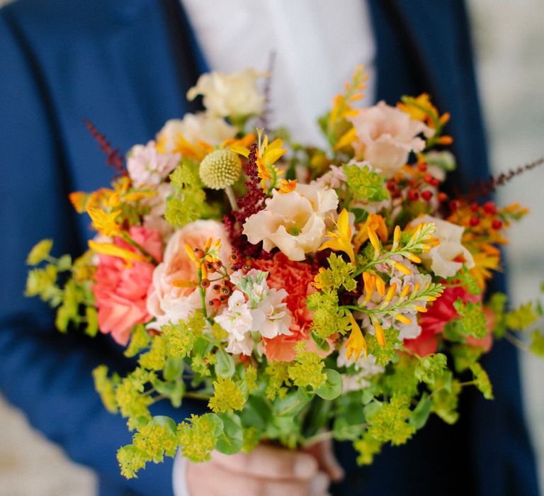 The groom holding a bouquet of green and pink wildflowers, including carnations and red berries