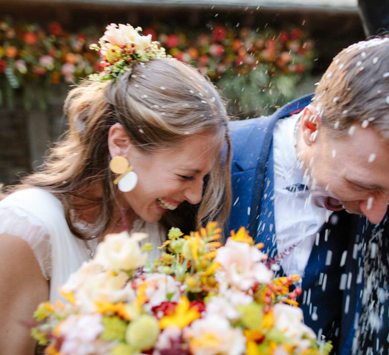 The bride and groom laughing as they have rice confetti thrown over them