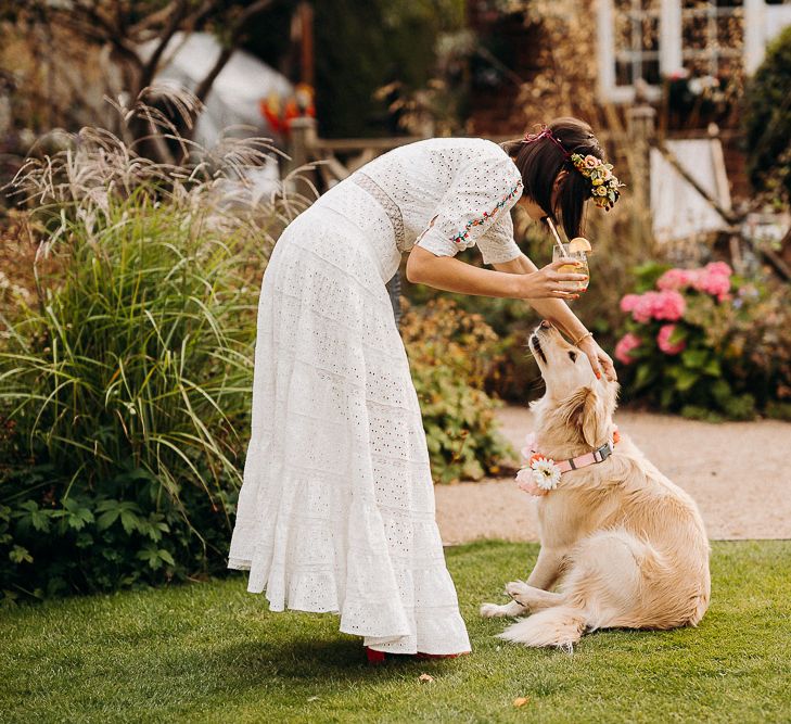 Bride in a bohemian dress patting her pet golden retriever