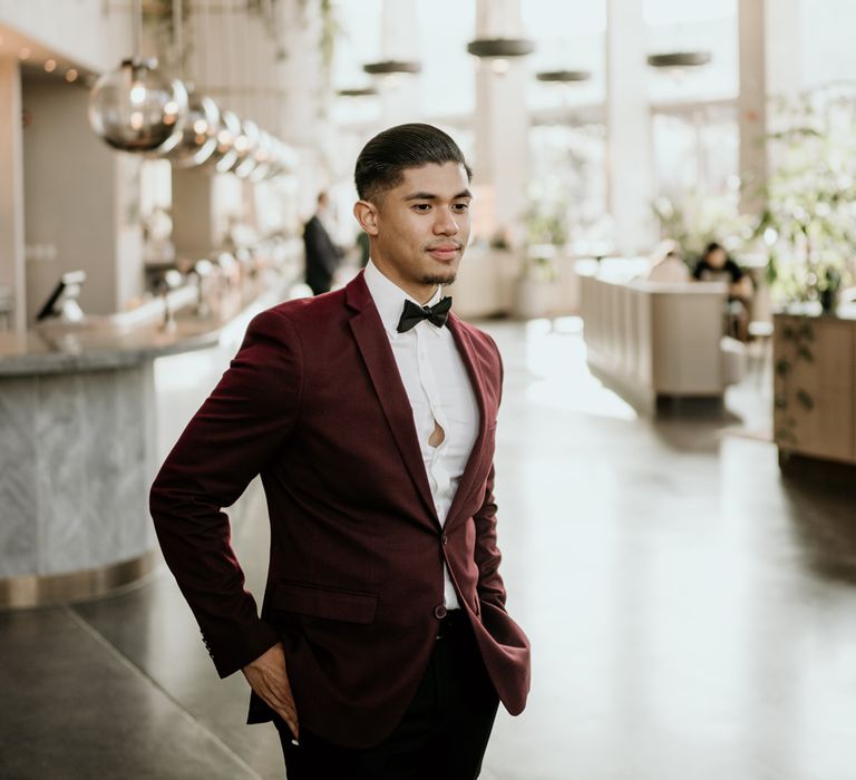 Stylish groom in black trousers, burgundy jacket and bow tie