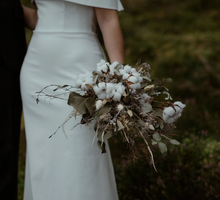 Bride carries white floral bouquet with green foliage