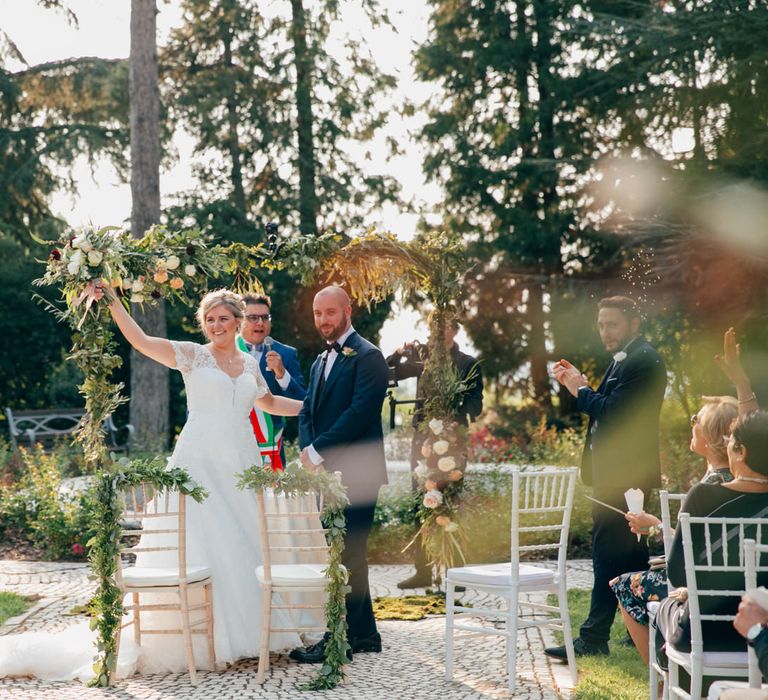 The guests clapping as the ceremony finishes, the bride is holding her bouquet in the air and smiling