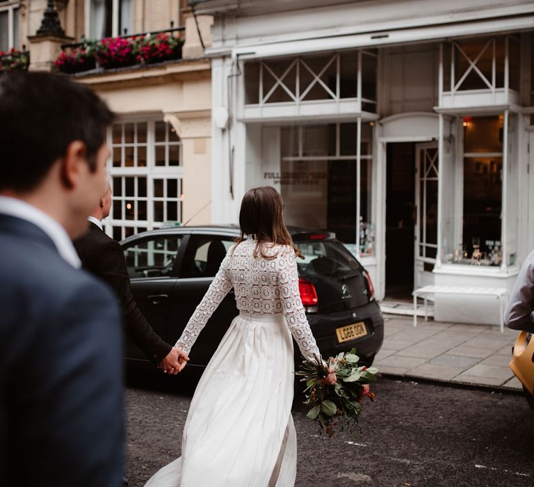 Bride in long sleeved lace Self Portrait wedding dress holding colourful bouquet walks through streets of Bristol holding hands with groom alongside two friends