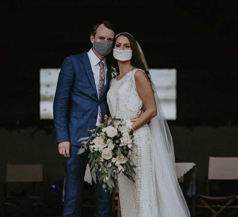 Bride & groom stand together whilst wearing face masks on the day of their wedding