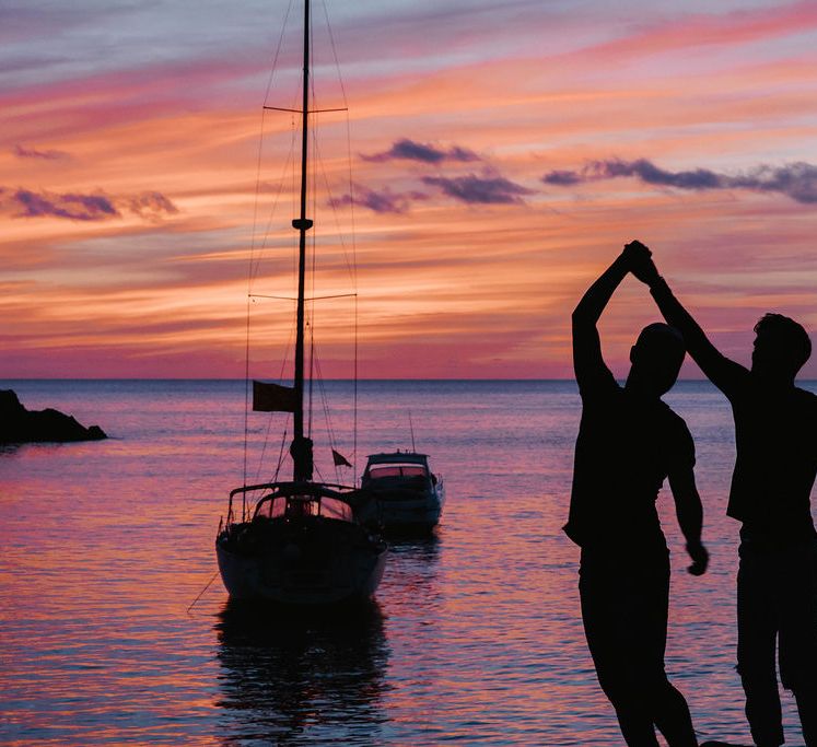 Grooms dance together as the sun sets behind the sea