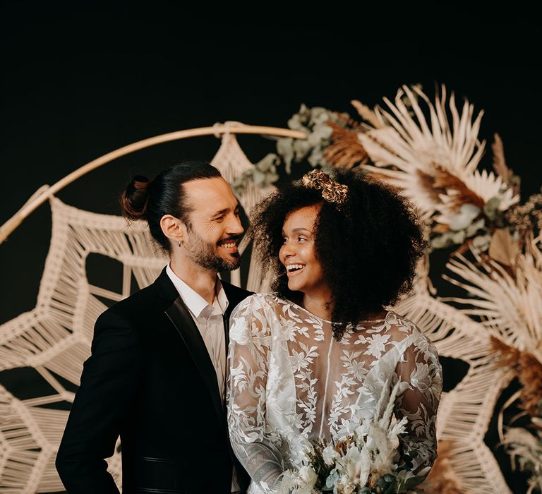 Bride & groom stand together in front of macrame backdrop 