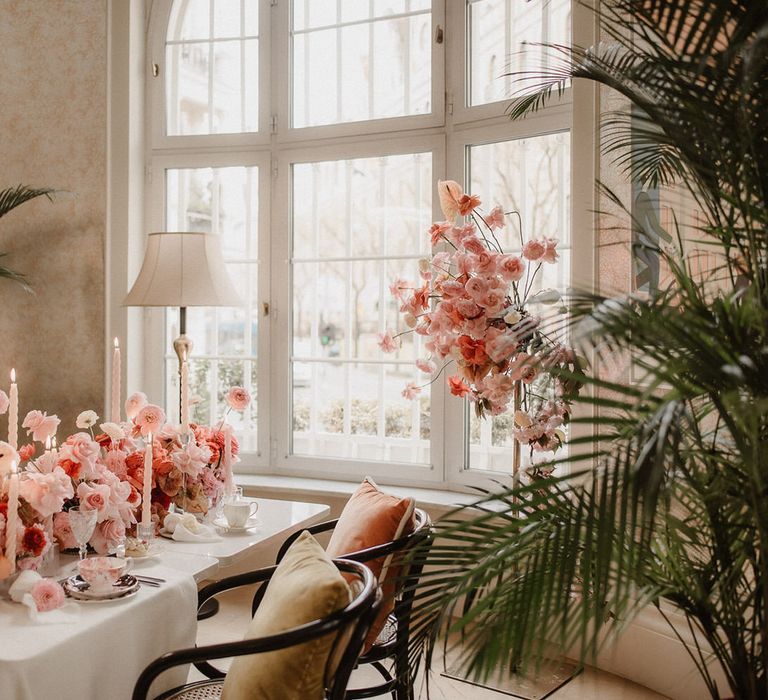 Luxurious peach wedding flowers tablescape with pink tapered candles, in between tropical palm tree plants with standing pink flower display