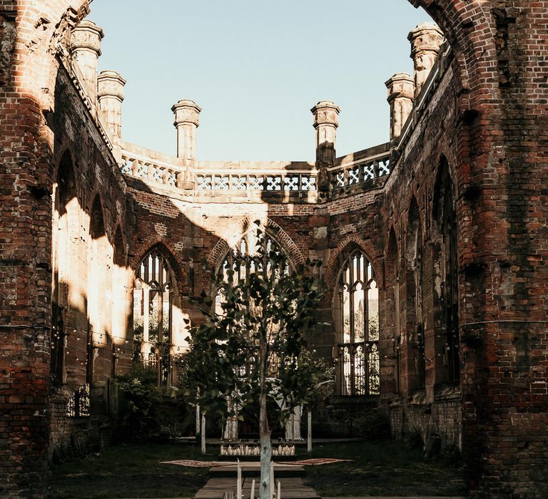 Wedding reception at St Lukes Bombed Out Church in Liverpool with greenery table runner, trees and pillar candle decor 