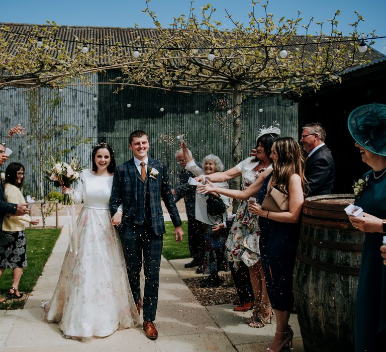 Confetti moments with bridesmaids green sparkly dresses, bride in a floral skirt dress and groom in a navy check suit 