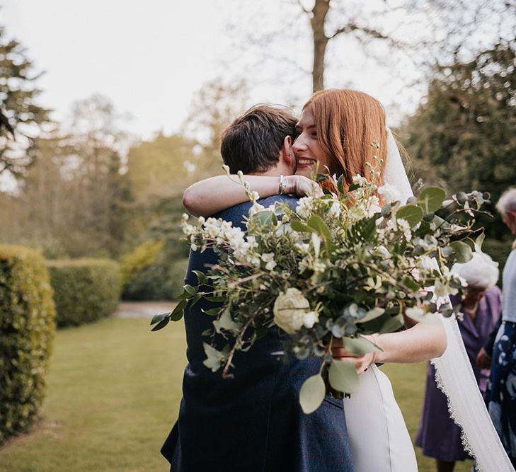 Bride holding a green and white oversized wedding bouquet and embracing her husband 