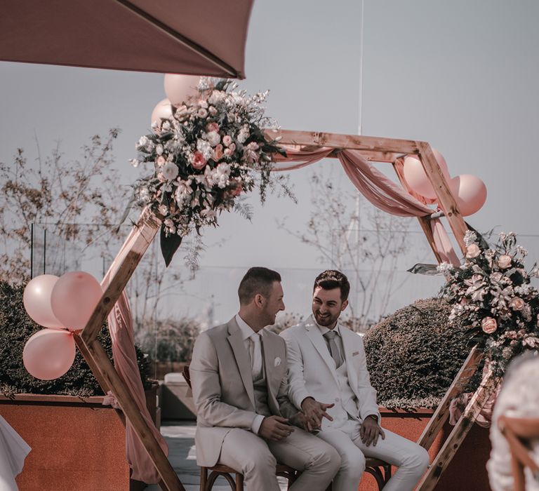 A gay couple sit under a hexagonal structure during their wedding ceremony.