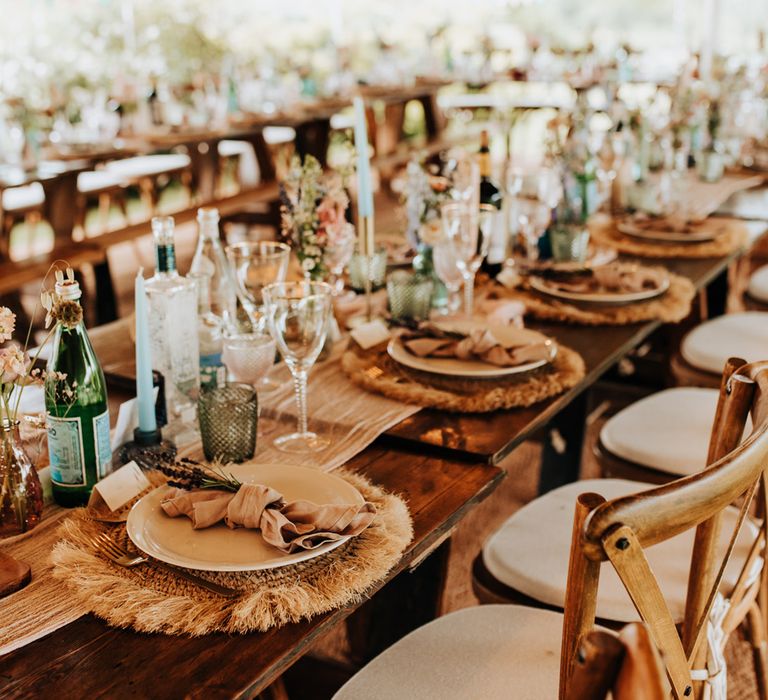 Rustic wedding table settings with dried flowers, bubble glasses and wooden chairs at wooden wedding breakfast table for garden wedding reception in tipi