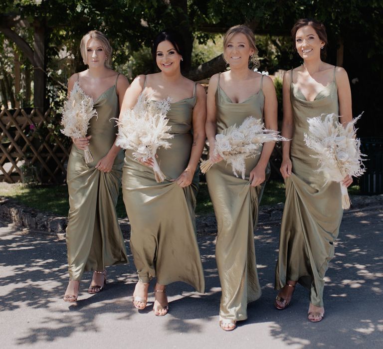 Bridesmaids in green satin midi dresses holding neutral beige dried flower bouquets 