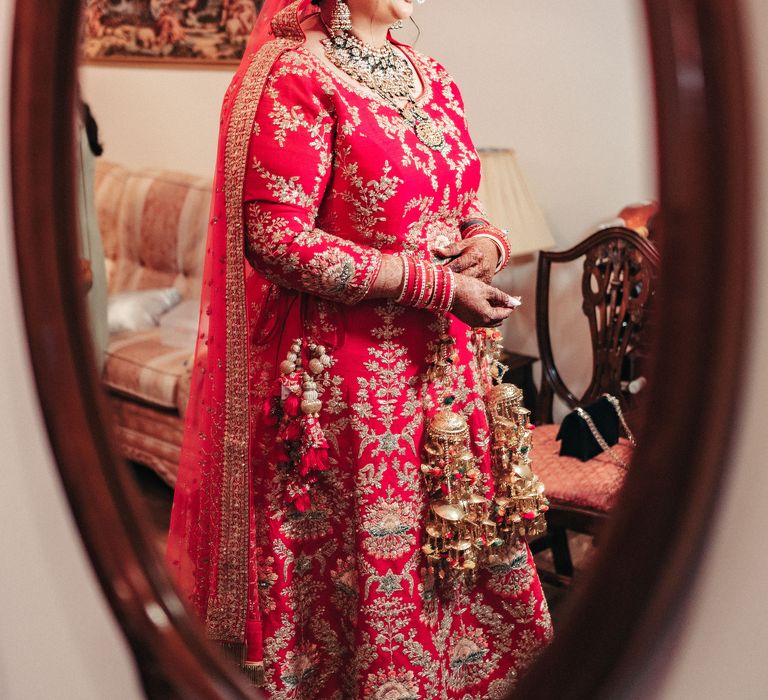 Bride stands in the mirror as she wears her traditional Lengha and gold jewellery 