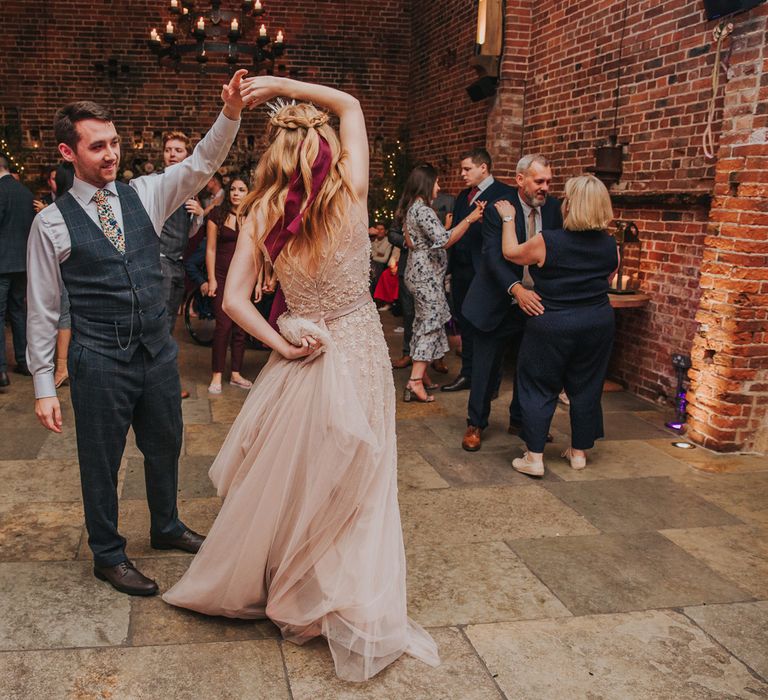 Groom in a grey check waistcoat and floral tie twirling his bride around on the dance floor in a pearl wedding dress at their Hazel Gap Barn wedding 