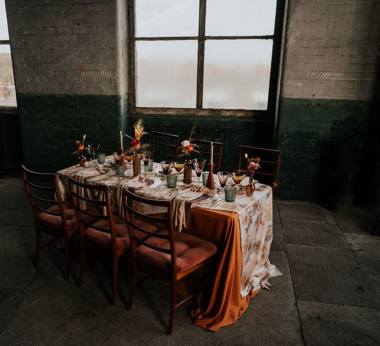 70s wedding table decor with patterned tablecloth, coloured glassware, and wildflowers 