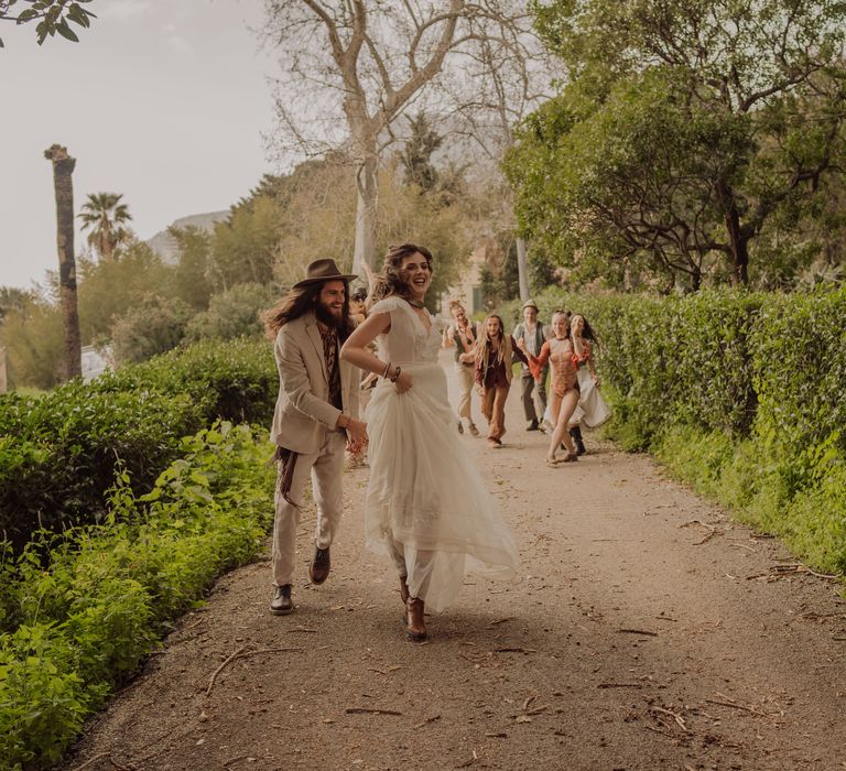 Bride & groom laugh and dance their way down path with circus performers following 