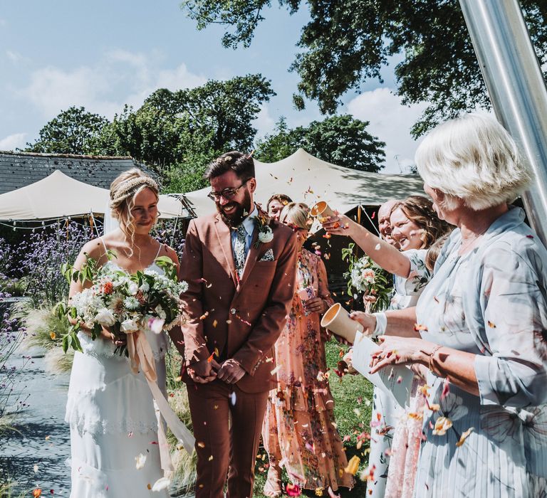 Bride & walk groom together outdoors on sunny day in Cornwall as bride carries floral bouquet