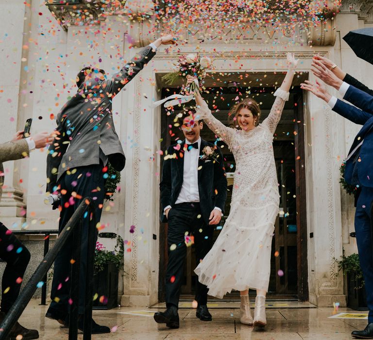 Bride celebrates with her arms in the air as she leaves Town Hall from wedding ceremony as confetti is thrown around her