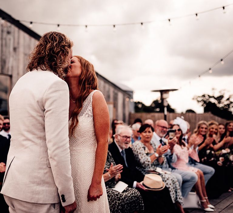 Bride and groom share their first kiss as a married couple under festoon lighting