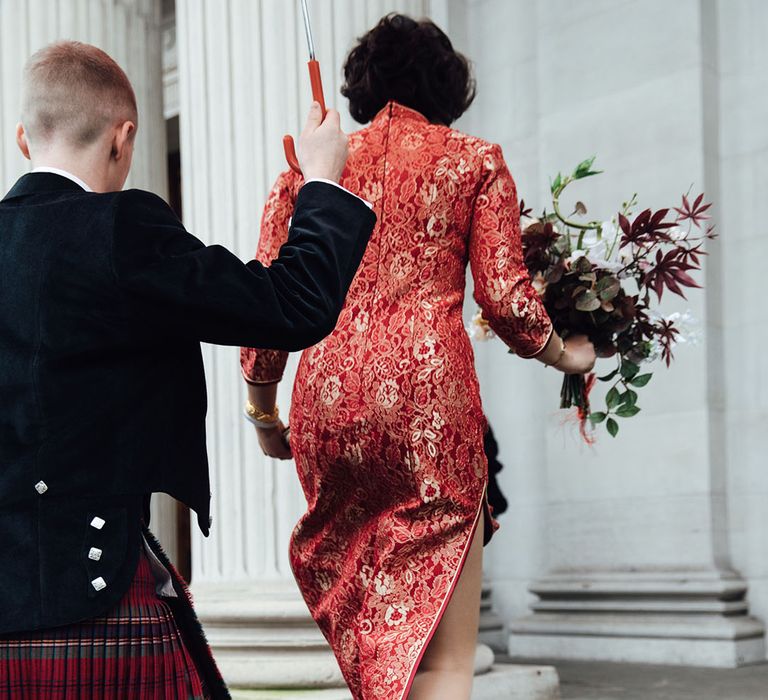 Groom carries umbrella over bride in red cheongsam dress