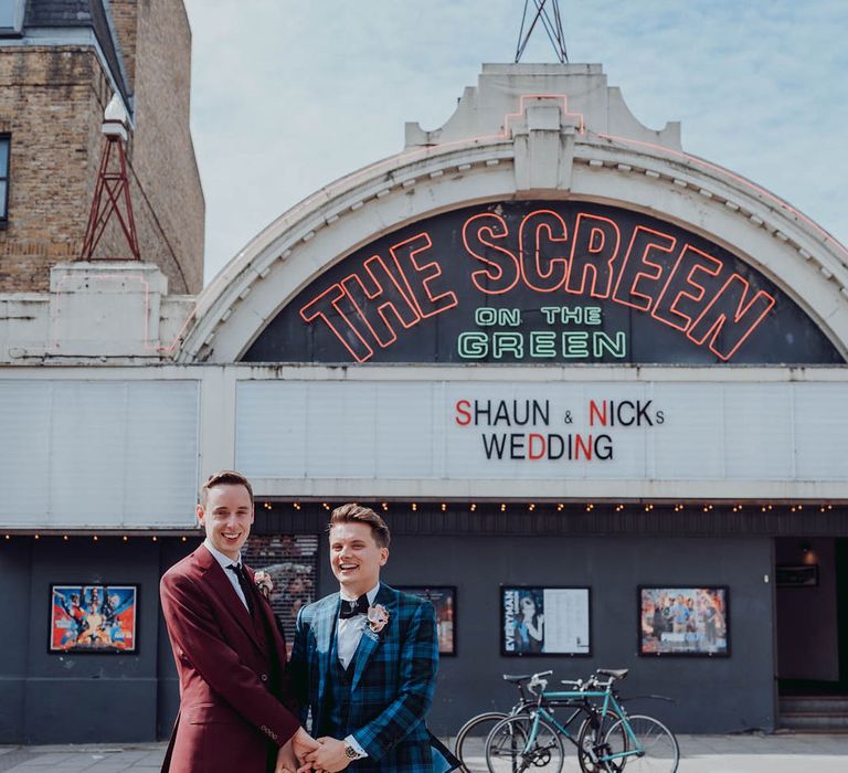 Grooms stand in front of cinema with their names across the front  | Kim Williams Weddings