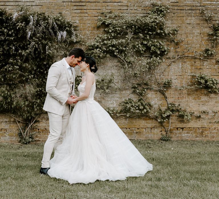 Portrait of a bride in a full skirt princess wedding dress and groom in a light suit on the grounds of Bylaugh Hall 