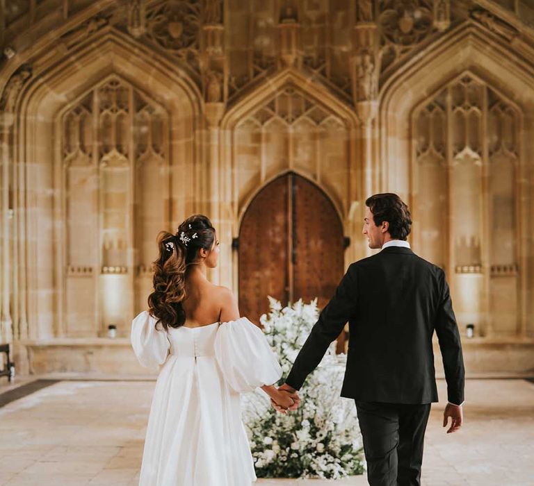 Groom in a black tuxedo holding hands with his bride at their monochrome Bodleian wedding reception