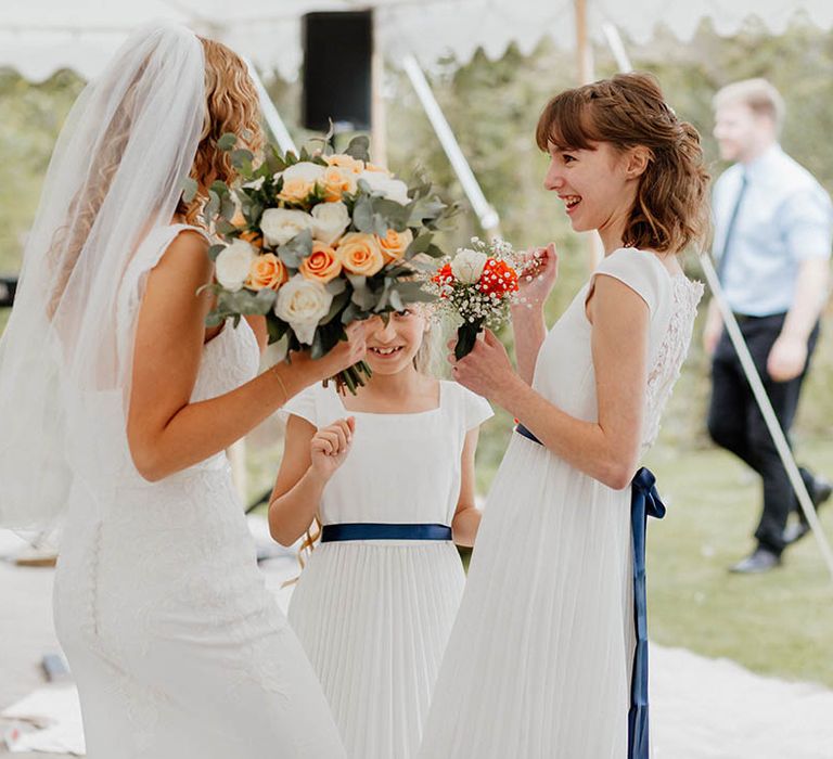 Bride stands with bridesmaids who wear white dresses complete with royal blue sashes 