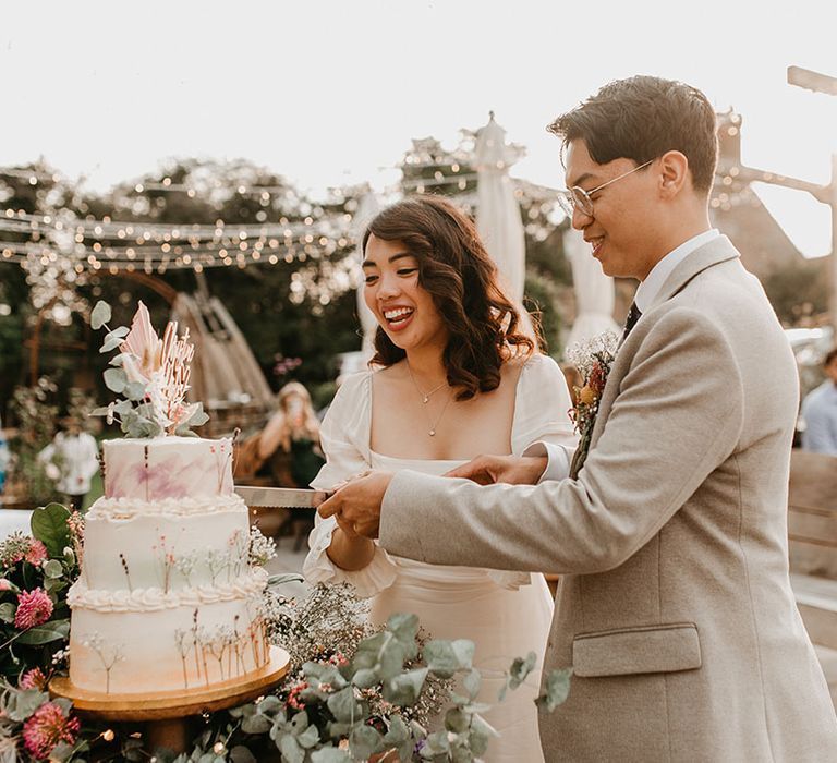 Bride & groom cut rustic wedding cake complete with floral decor