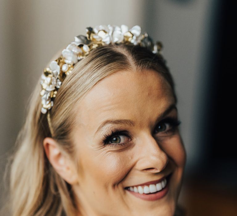 Bride with curled hair and floral headband smiles at the camera before wedding