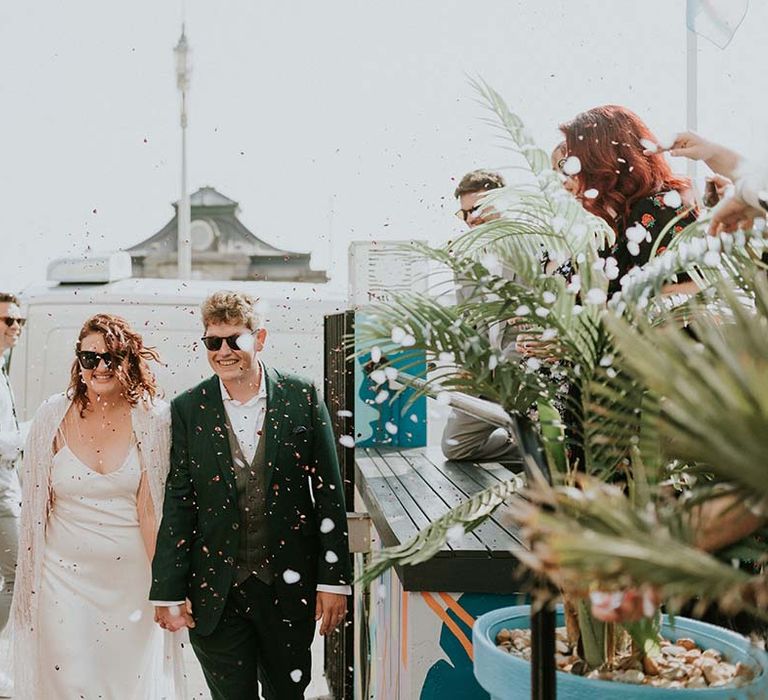 Bride & groom walk through confetti whilst wearing sunglasses on their wedding day