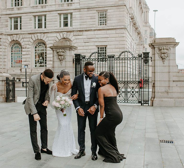 Bride & groom laugh with their wedding party on their wedding day outdoors