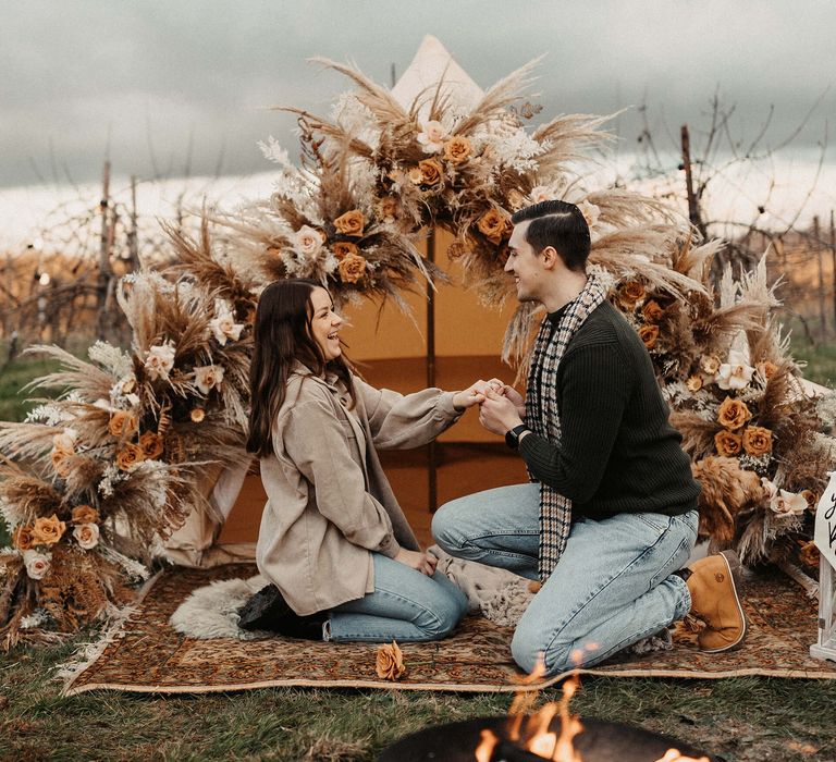 Man in jeans and a tartan scarf proposing to his partner in front of a boho bell tent 