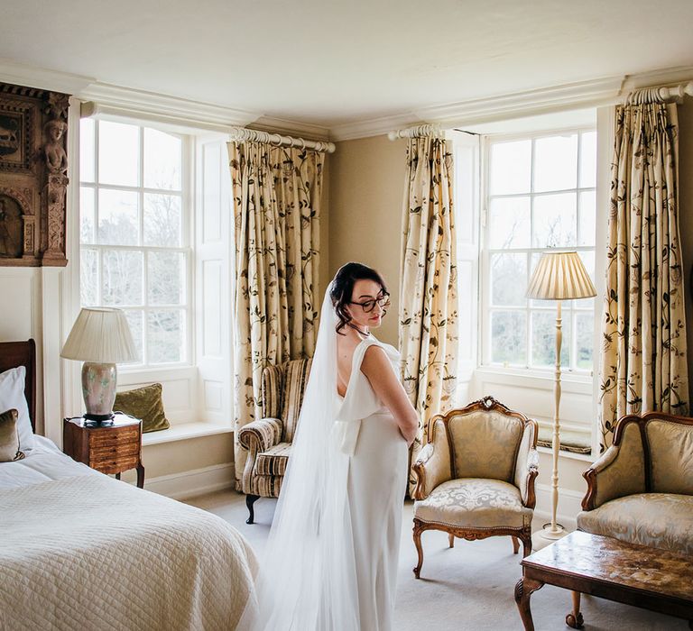 Bride stands in the middle of room wearing bridal gown and veil