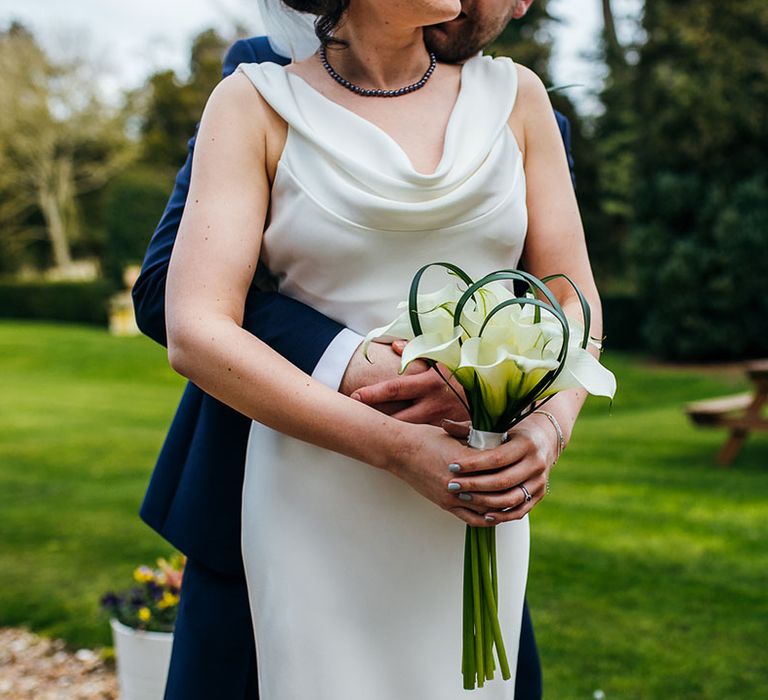 Bride wears cowl neck wedding gown complete with bouquet filled with lilies