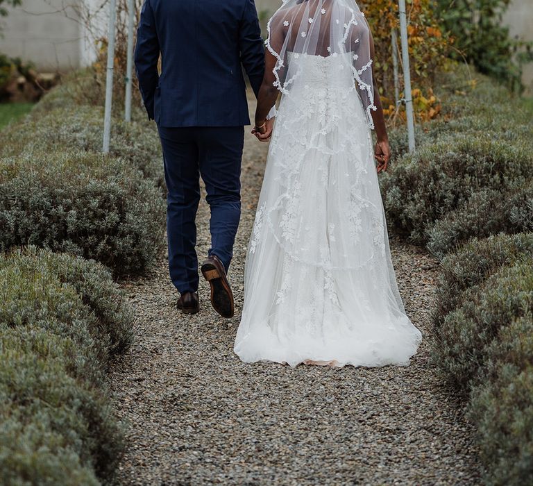 Lace edge wedding veil hangs as bride holds the grooms hand in outdoor nature setting